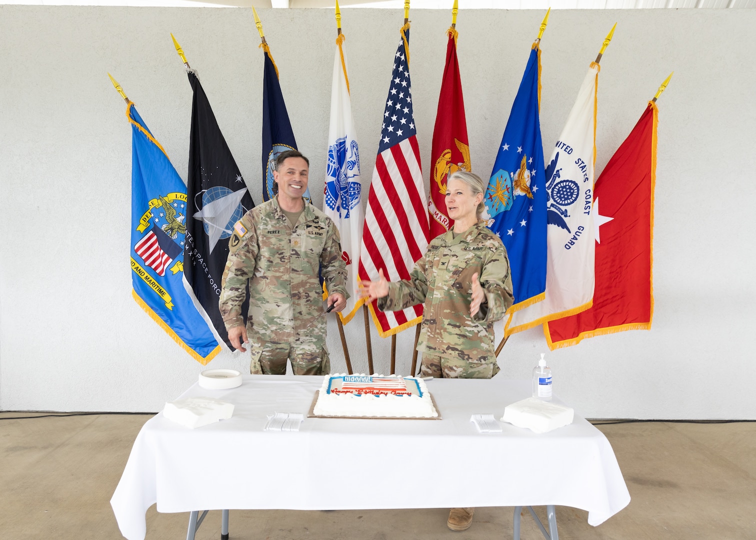 two people in military uniform stand before a cake on a table.