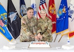two people in military uniform prepare to cut a cake. One is a woman and the other a man.