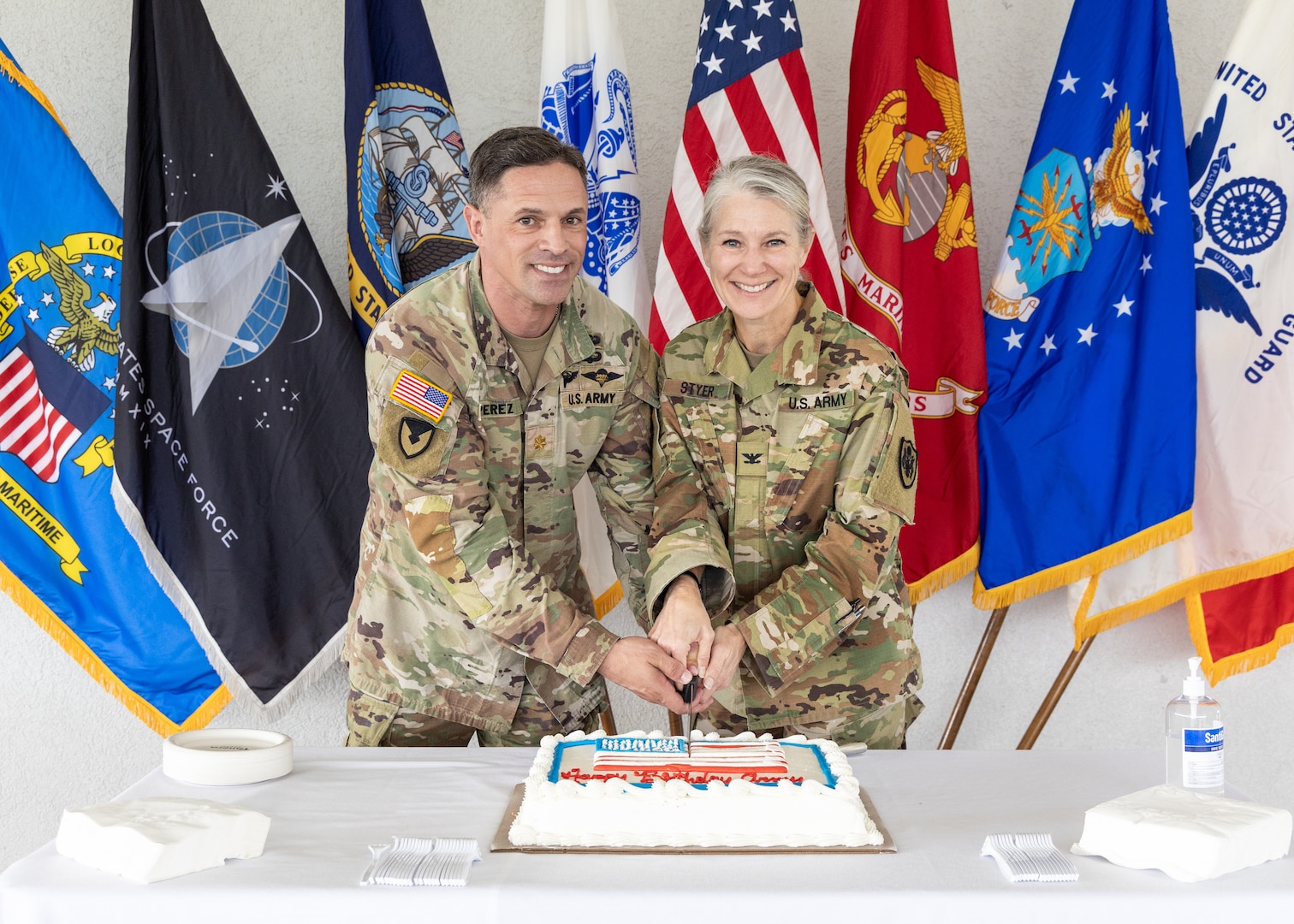 two people in military uniform prepare to cut a cake. One is a woman and the other a man.