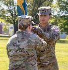 One female Soldier passes a battalion flag outdoors.