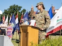 Women in Army uniform addresses an audience during a Change of Command Ceremony outdoors.