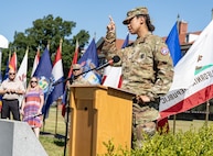 Women in Army uniform addresses an audience during a Change of Command Ceremony outdoors.