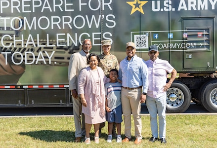 Female Soldier stands outdoors in front of a truck with his family.