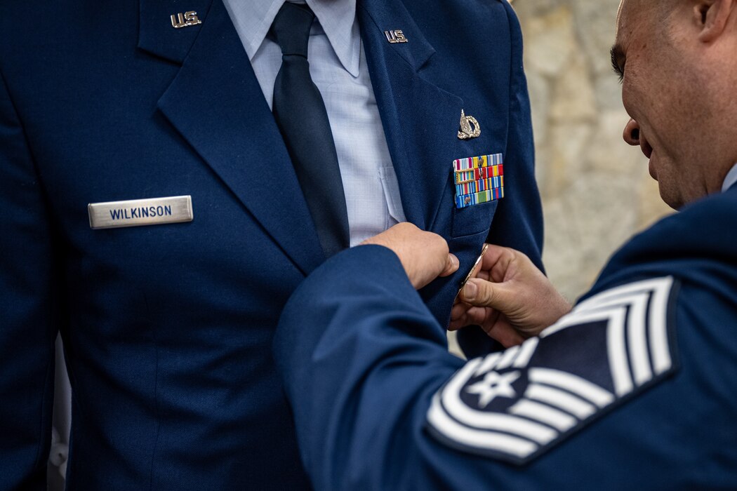 A closeup photo of a Chief Master Sgt pinning a badge onto an officer's service coat