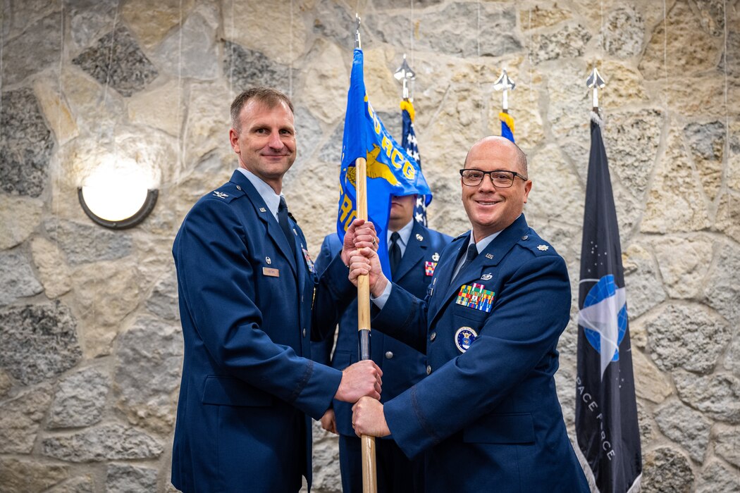 Col Brown and Lt. Col. Hatchley pose for a photo holding a guidon with unit blue banner