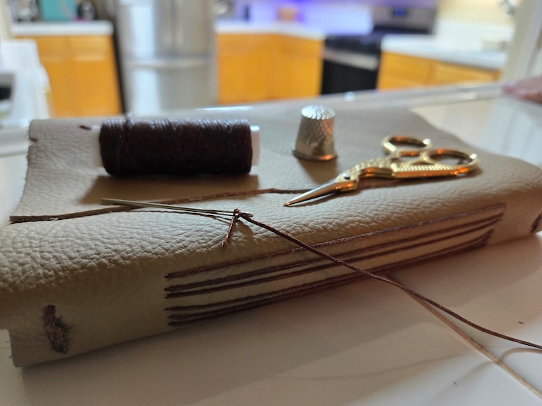 handmade leatherbound book with string, thimble, and scissort sitting on top