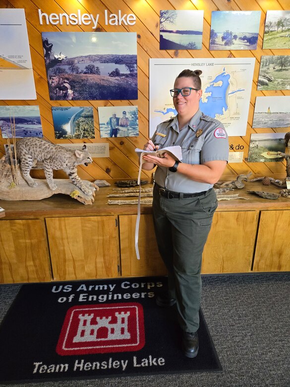 Lead natural resource specialist Shawna Polen stands in front of a interactive display for Hensley Lake holding a handmade letherbound book she created for a sustainable art challenge.