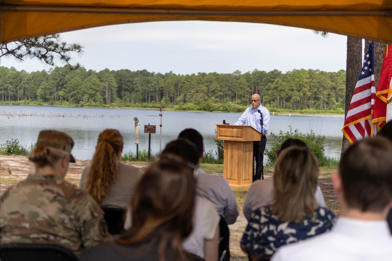 A man in civilian attire stands at a lectern outdoors.