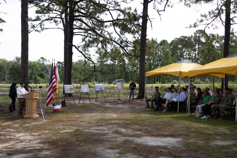 A man in civilian attire stands at a lectern outdoors.
