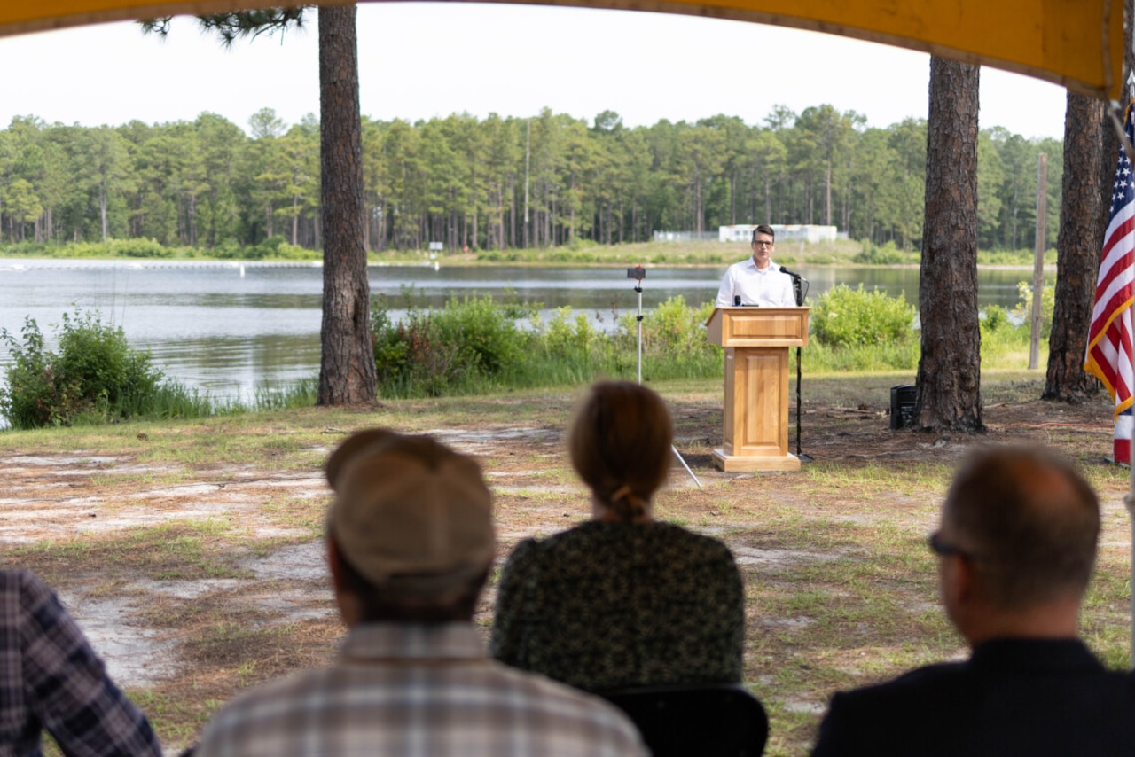 A man in civilian attire stands at a lectern outdoors.