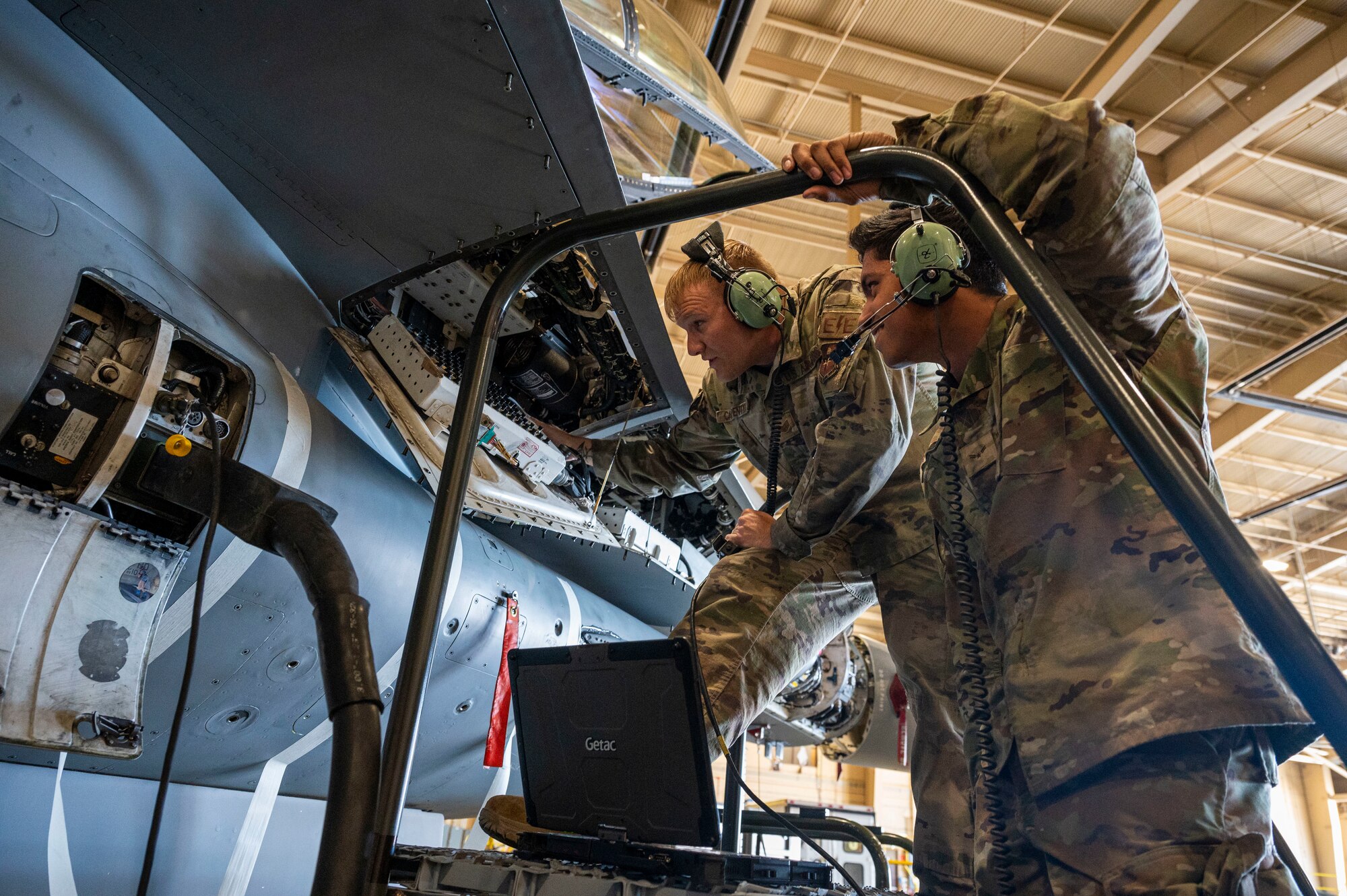 U.S. Air Force Staff Sgt. Cody Carpenter, 49th Component Maintenance Squadron electrical environmental systems craftsman, center, and U.S. Air Force Airman 1st Class Alejandro Esparza, 49th CMS electrical environmental systems journeyman, test the capabilities of a  modified communications W cords at Holloman Air Force Base, New Mexico, May 20, 2024. Allowing up to three aircrew members to speak with a pilot, the W cord can be used to train newer personnel and troubleshoot any discrepancies that may occur during operations. (U.S. Air Force photo by Senior Airman Isaiah Pedrazzini)