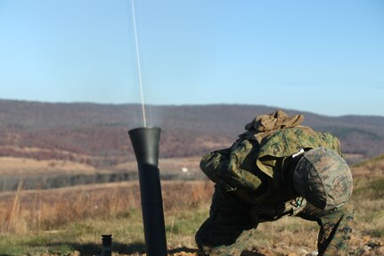 A Marine crouches down and turns away from a tube as it emits a beam of light.