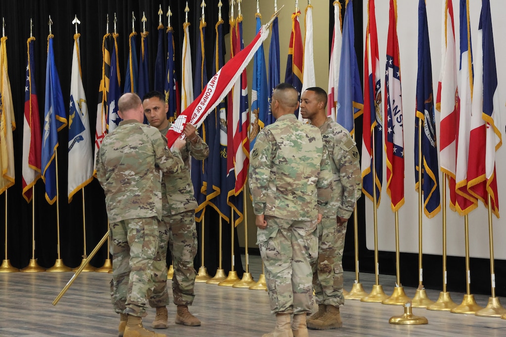 ChatGPT
Four U.S. uniformed male soldiers standing in a circle, one passing a long gold flagpole wrapped with a red flag with white fringe wrapped to another soldier.