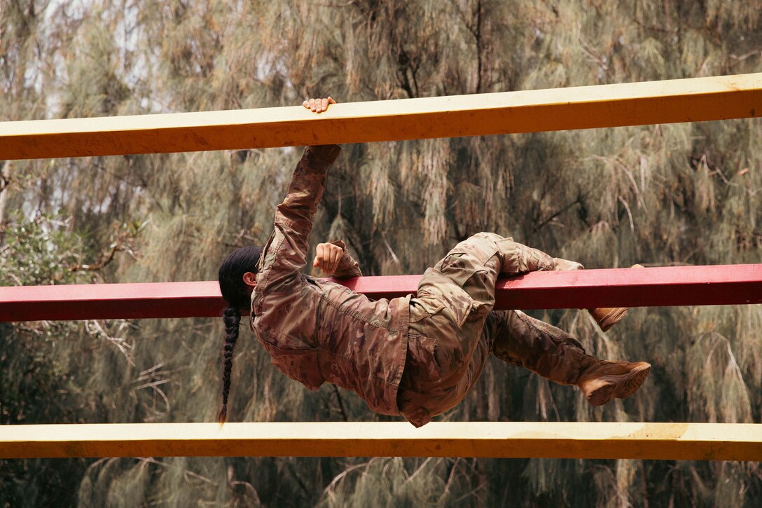 A soldier climbs a horizontal fence during a competition.