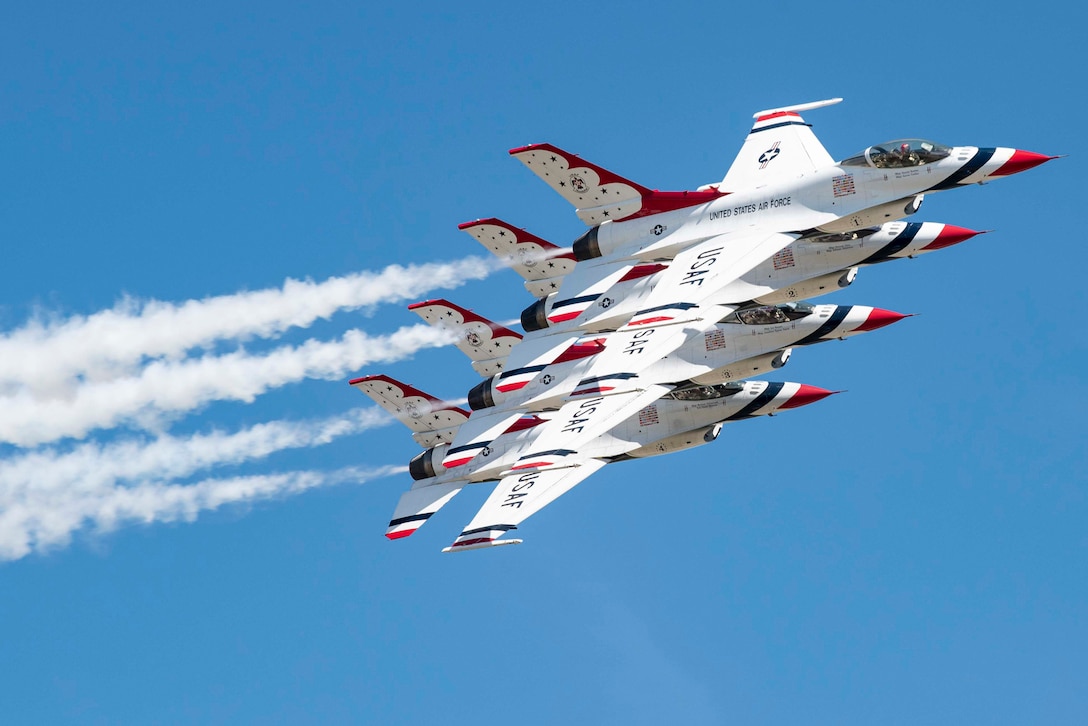 Four military aircraft fly in close formation during a daylight air show, leaving vapor trails.