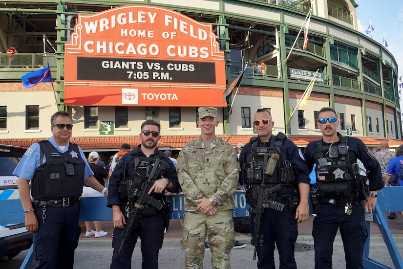 Lt. Col Brian Dunn, Public Affairs Officer, 85th U.S. Army Reserve Support Command, stands with Chicago police officers in front of the iconic Wrigley Field marquee, June 17,2024. The Chicago Cubs honored Dunn during their Military Salute at their home game versus the San Francisco Giants.