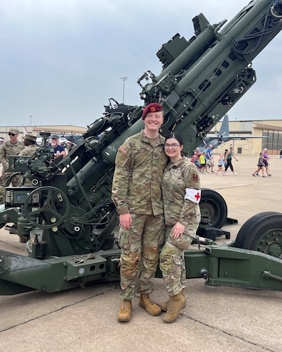 An Airman and a soldier stand in front of a howitzer