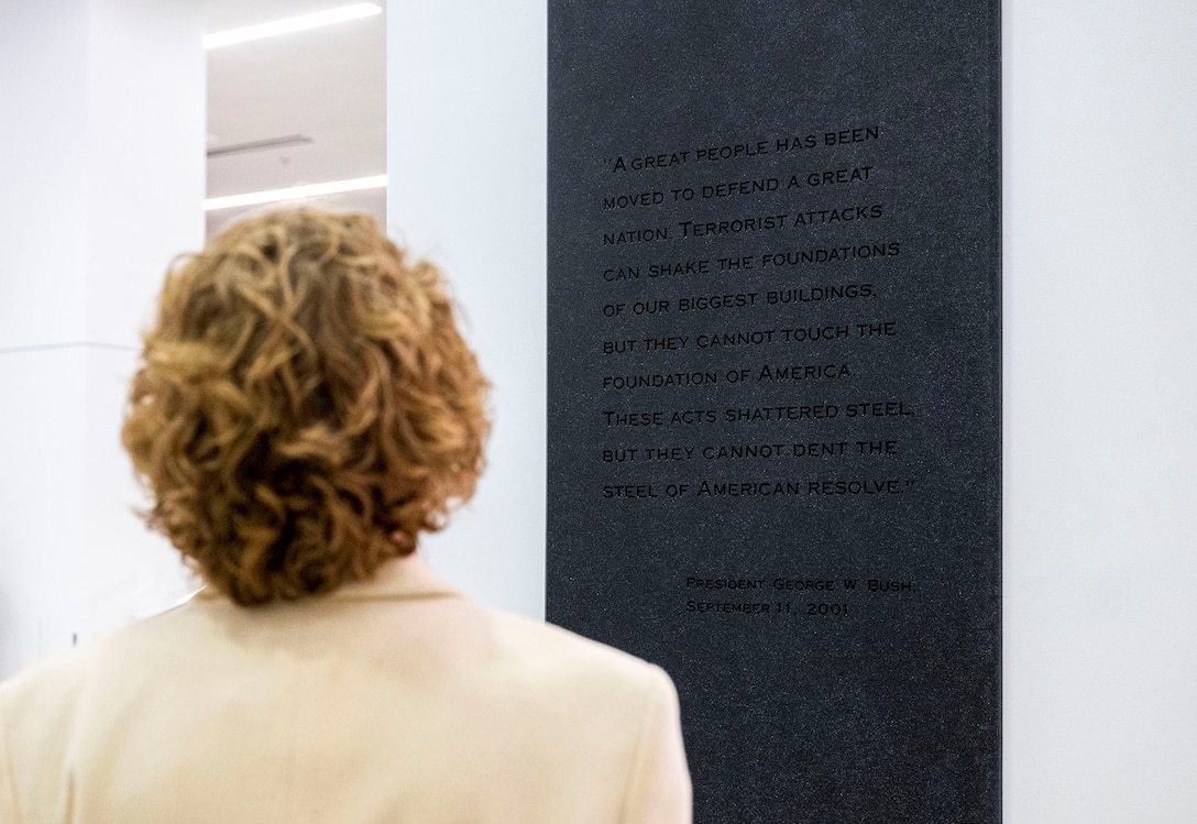 A woman in a cream jacket faces away from the camera as she reads a quote commemorating 9/11 victims on a slate display.