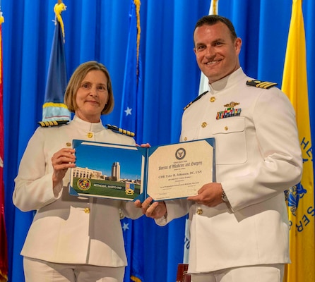 240607-N-JC800-1152 BETHESDA, Md. (Jun. 7, 2024) – Capt. Katharne Shobe, commanding officer of Naval Medical Leader and Professional Development Command, presents Cmdr. Tyler Johansen with his certificate of completion of his residency training in Periodontics during the graduation ceremony for the Naval Postgraduate Dental School. (U.S. Navy photo by Mass Communication Specialist 1st Class Heath Zeigler/Released)