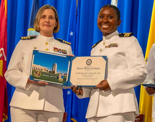 240607-N-JC800-1178 BETHESDA, Md. (Jun. 7, 2024) – Capt. Katharne Shobe, commanding officer of Naval Medical Leader and Professional Development Command, presents Cmdr. Opeyemi Fadoju with her certificate of completion of his residency training in Comprehensive Dentisry during the graduation ceremony for the Naval Postgraduate Dental School. (U.S. Navy photo by Mass Communication Specialist 1st Class Heath Zeigler/Released)