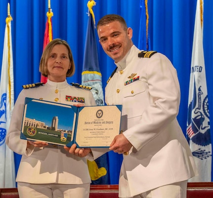 240607-N-JC800-1181 BETHESDA, Md. (Jun. 7, 2024) – Capt. Katharne Shobe, commanding officer of Naval Medical Leader and Professional Development Command, presents Cmdr. Jesse Froehner with his certificate of completion of his residency training in Comprehensive Dentistry during the graduation ceremony for the Naval Postgraduate Dental School. (U.S. Navy photo by Mass Communication Specialist 1st Class Heath Zeigler/Released)