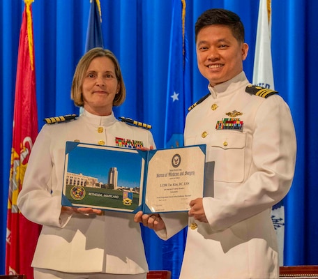 240607-N-JC800-1203 BETHESDA, Md. (Jun. 7, 2024) – Capt. Katharne Shobe, commanding officer of Naval Medical Leader and Professional Development Command, presents Lt. Cmdr. Tae Kim with his certificate of completion of his residency training in Endodontics during the graduation ceremony for the Naval Postgraduate Dental School. (U.S. Navy photo by Mass Communication Specialist 1st Class Heath Zeigler/Released)