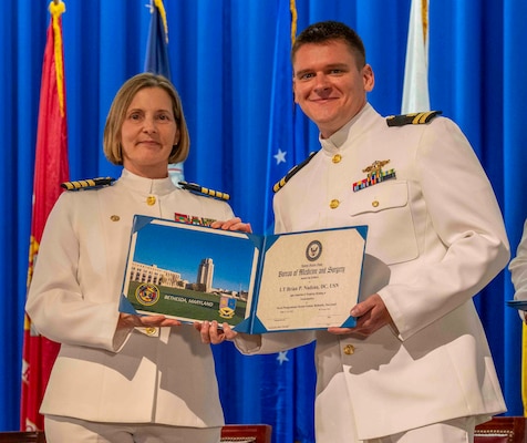 240607-N-JC800-12018BETHESDA, Md. (Jun. 7, 2024) – Capt. Katharne Shobe, commanding officer of Naval Medical Leader and Professional Development Command, presents Lt. Brian Nadeau with his certificate of completion of his residency training in Endodontics during the graduation ceremony for the Naval Postgraduate Dental School. (U.S. Navy photo by Mass Communication Specialist 1st Class Heath Zeigler/Released)