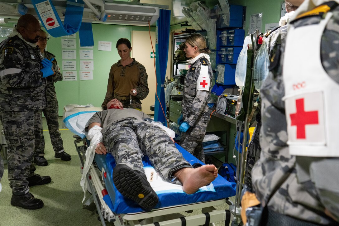 U.S. Navy Lt. Cmdr. Athena Mikros, center, an emergency physician with Combat Logistics Battalion 5 (Reinforced), Marine Rotational Force – Darwin 24.3, and Royal Australian Navy medical personnel assigned to HMAS Adelaide (L01) discuss medical treatment for a simulated burn patient during a damage control exercise aboard HMAS Adelaide (LO1), in the Coral Sea, June 6, 2024. Marines and Sailors embarked on HMAS Adelaide (L01) alongside their Australian Allies to participate in the Wet and Dry Exercise Rehearsal, transiting from Darwin to Townsville from June 2-20, 2024. During WADER, elements from the MRF-D Marine Air-Ground Task Force will conduct MV-22B Osprey deck landing qualifications, a live-fire deck shoot, medical subject matter expert exchanges, enhance amphibious fires, command and control, and initiate a ship-to-shore movement in order to set conditions for future operational tasking. Mikros is a native of Illinois. (U.S. Marine Corps photo by Gunnery Sgt. Kassie McDole)