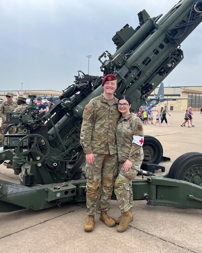 An Airman and a soldier stand in front of a howitzer