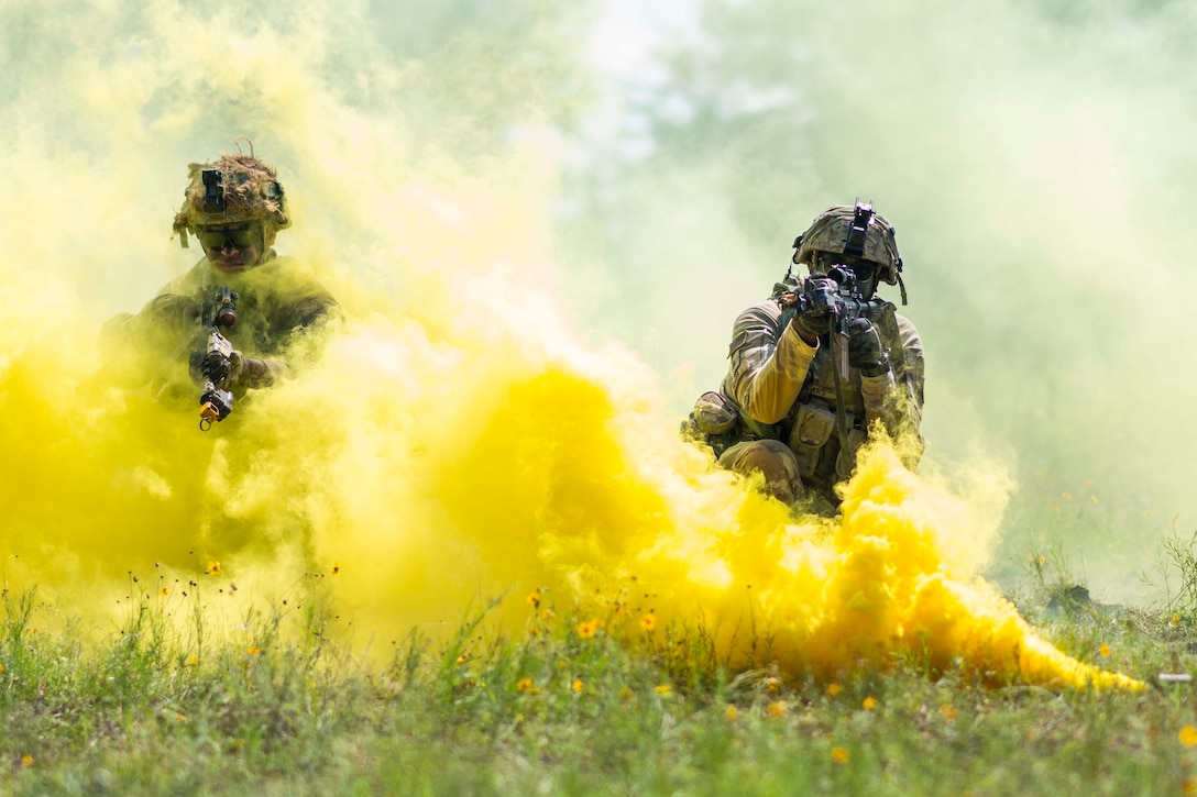 Two soldiers point weapons from behind billows of yellow smoke.