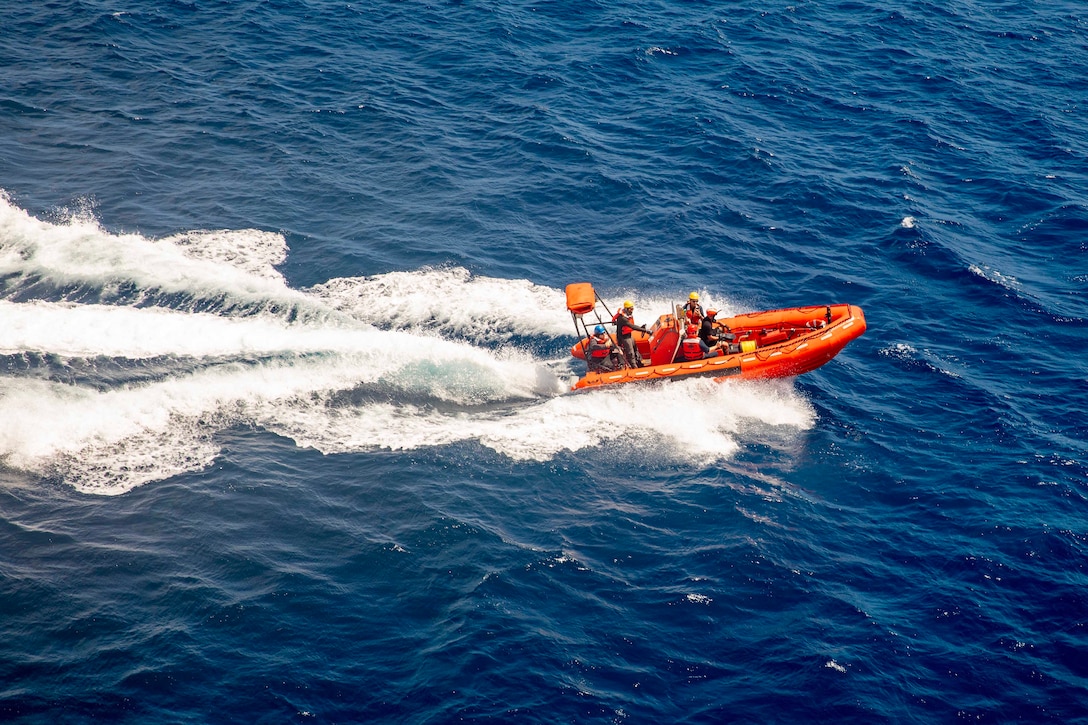 A large inflatable boat with five sailors on board skims across a dark blue ocean.