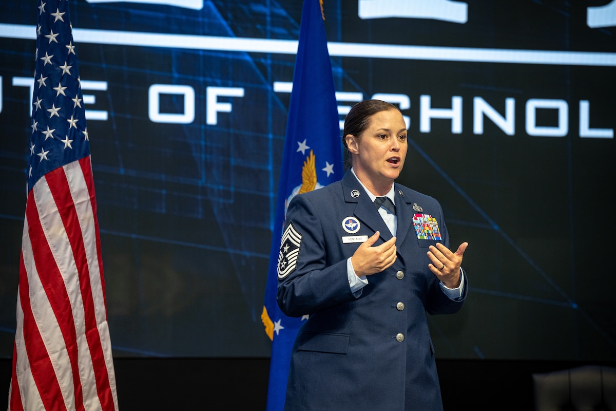 Chief Master Sgt Fontaine gives a speech while on stage with flags behind her