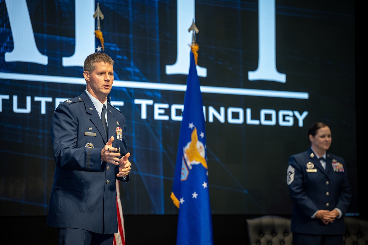 Col Richards gives a speech standing on stage with Chief Master Sgt Fontaine in the background