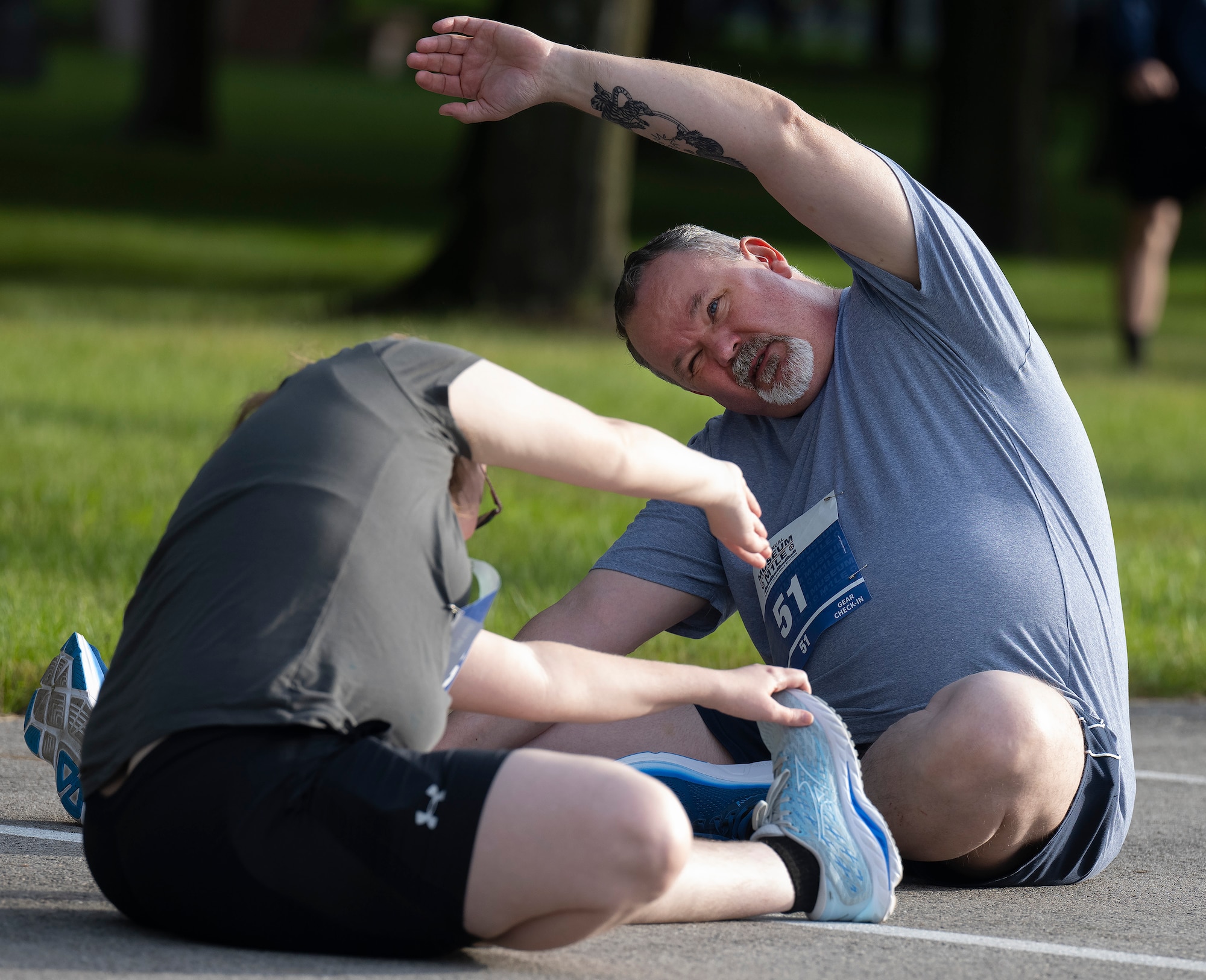 A man and a woman sit on the ground stretching facing each other.
