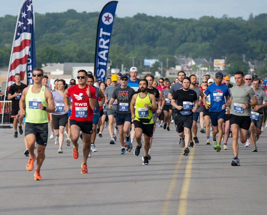 A large group of runners run towards the camera. In the background is a blue banner the says "start".