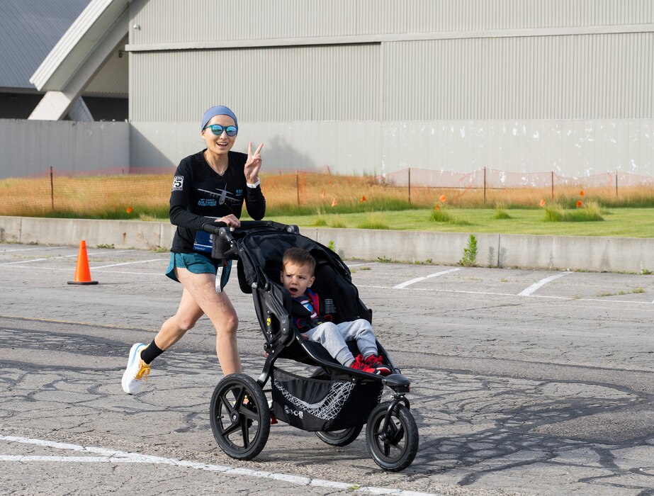 A runner flashes a peace sign as she pushes a small boy in a stroller.