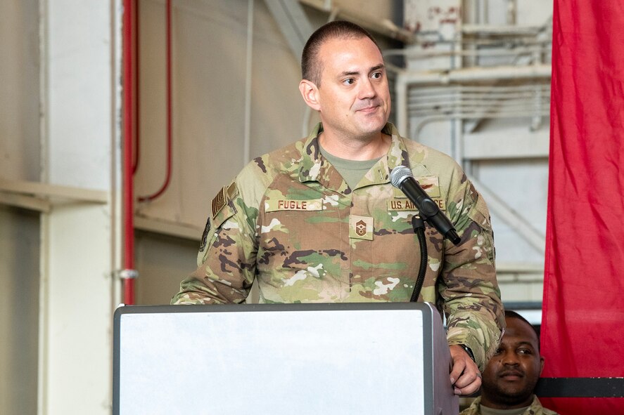 A man in military uniform leans on a wooden podium while speaking into a microphone.