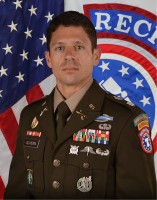 Photo of Army Lt. Col. wearing Army Green Service Uniform while posing in front of the American flag & United States Recruiting Command (USAREC) flag.