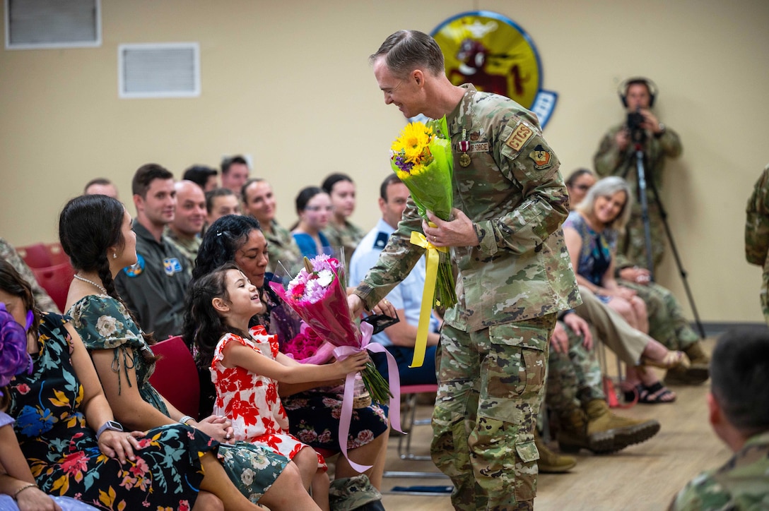 An airman gives flowers to seated family members as an audience watches.