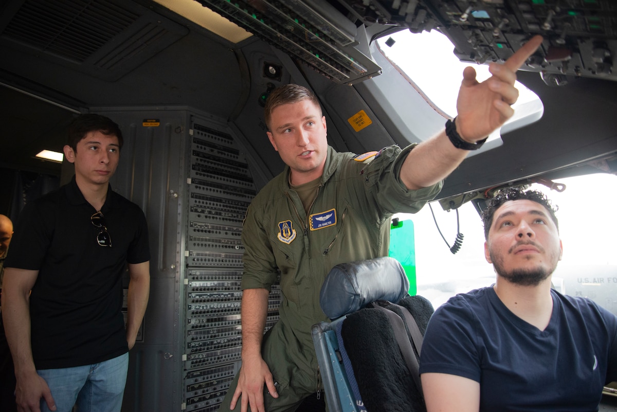 Air Force captain in flight suite shows two students the aircraft cockpit.