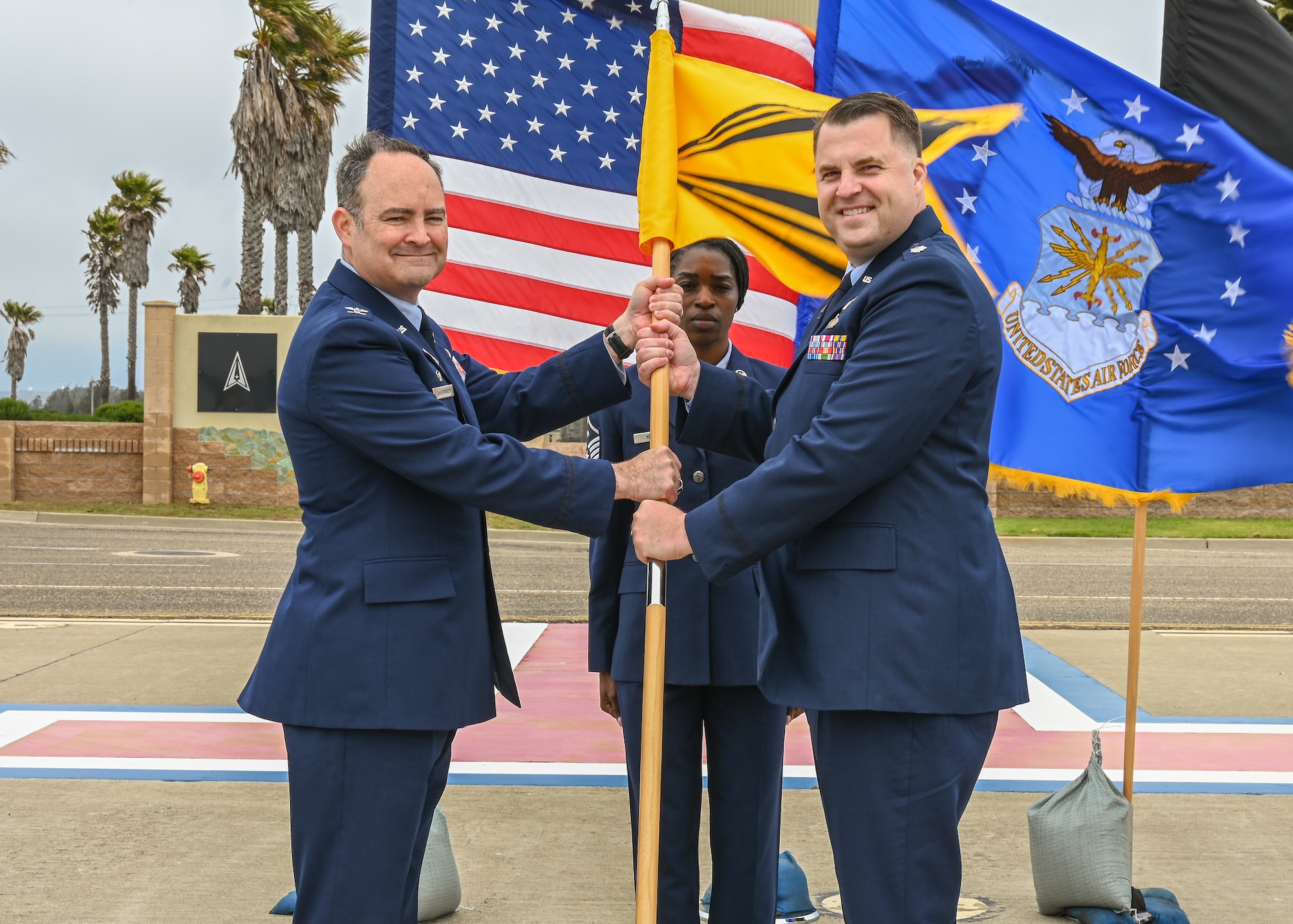 Space Launch Delta 30 commander, left, passes the 2nd Space Launch Squadron flag to 2nd Space Launch Squadron incoming commander, right, during the 2nd SLS change of command ceremony at Vandenberg Space Force Base.