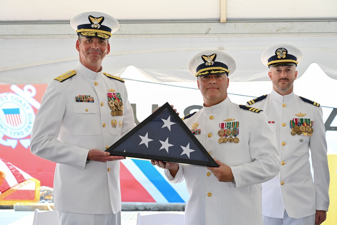 Vice Adm. Nathan Moore, Atlantic Area commander, left, poses for a photo with Cmdr. Aaron Kowalczk, commanding officer of U.S. Coast Guard Cutter Dauntless (WMEC 624), June 21, 2024, with the national ensign of Dauntless during a heritage recognition ceremony held for the cutter in Pensacola, Florida. Dauntless was recognized for 56 years of service to the nation in the presence of current and former crew members, family, and friends before it was placed in commission, special status. (U.S. Coast Guard photo by Petty Officer 2nd Class Brandon Hillard)