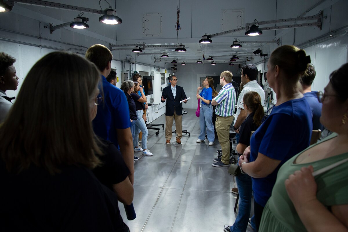 Students stand inside the operating room of the centrifuge. Man talks to the students.