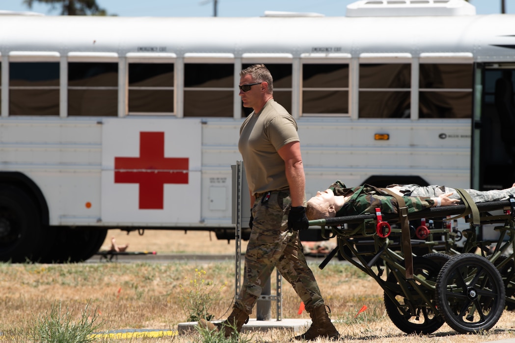 An airman wheels a simulated patient in front of an ambulance bus