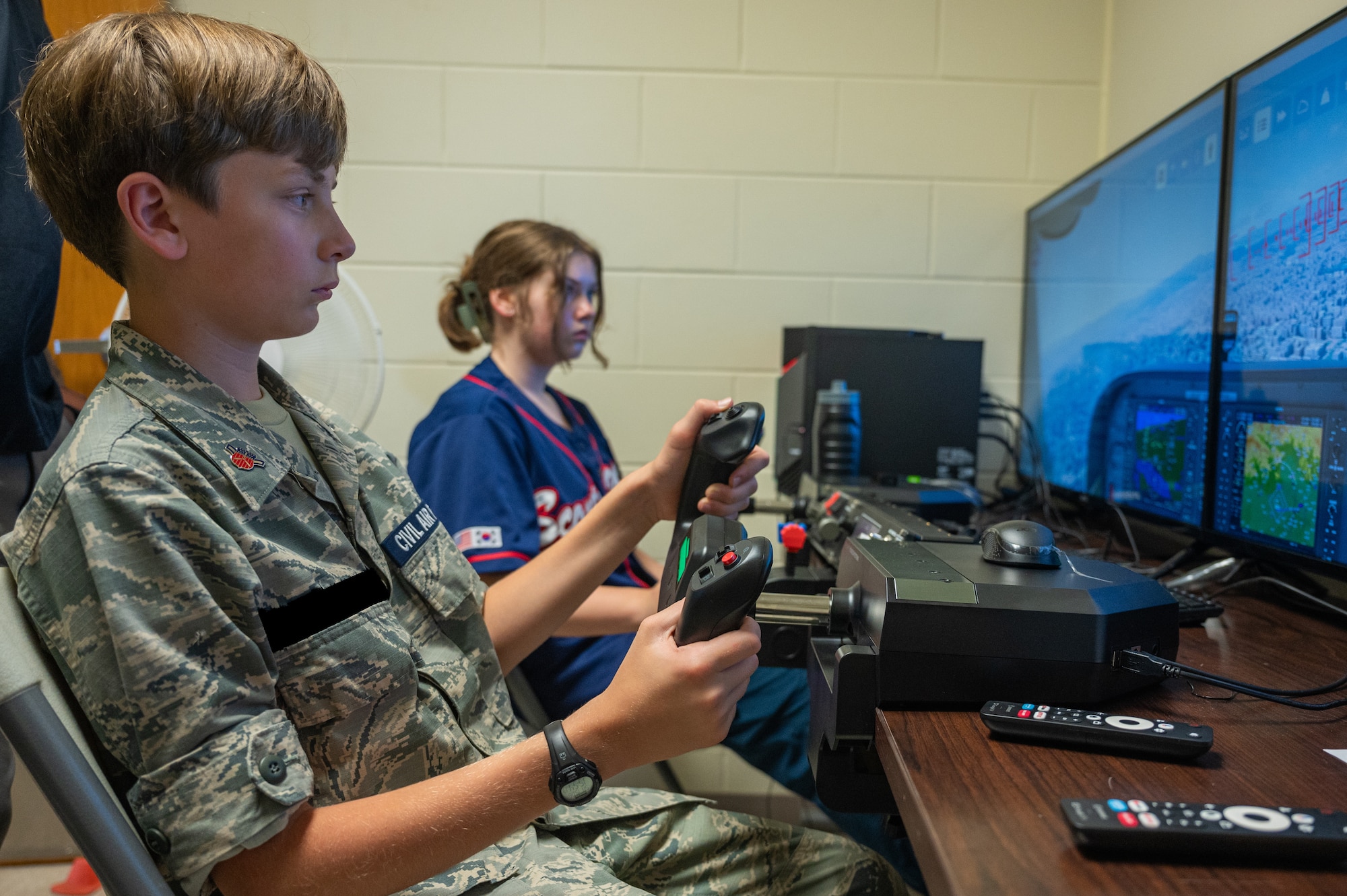 A Civil Air Patrol cadet, Squadron NHQ-127, left, and a girl scout from the Daegu Scouts BSA, use a flight simulator during a youth aviation day at Osan AB, Republic of Korea, June 15, 2024. The CAP Squadron gathered U.S. and Korean scouts at Osan AB in a ROK-U.S. friendship event centered around aviation. (U.S. Air Force photo by Airman 1st Class Chase Verzaal) (This photo has been altered for security purposes.)