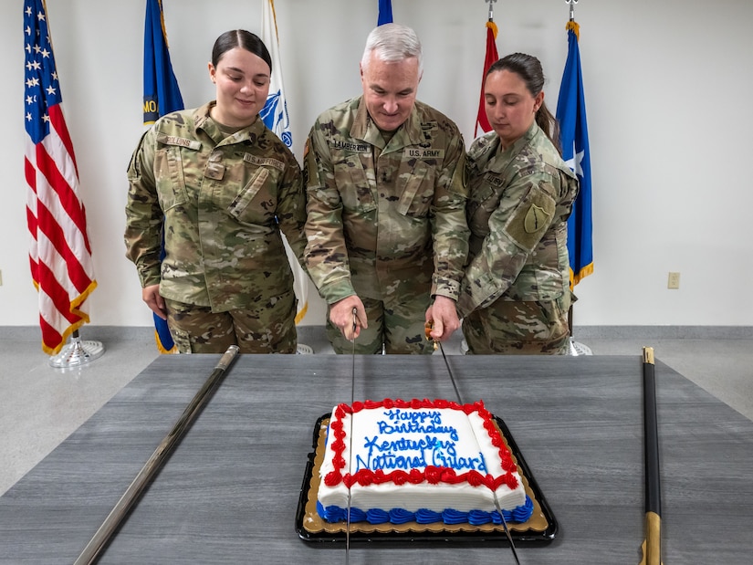 U.S. Air Force Airman Makenna Rollins, left, a supply technician in the Kentucky Air National Guard, and U.S. Army Sgt. Jensen Humphrey, right, a paralegal specialist in the Kentucky Army National Guard, assist U.S. Army Maj. Gen. Haldane Lamberton, adjutant general of the Commonwealth of Kentucky, in cutting a cake to mark the 232nd birthday of the Kentucky Guard during a ceremony at the Kentucky Air National Guard Base in Louisville, Ky., June 20, 2024. The Kentucky Guard, which was established by Gov. Isaac Shelby on June 24, 1792, is comprised of more than 6,000 Soldiers and over 1,100 Airmen stationed across the Commonwealth. (U.S. Air National Guard photo by Dale Greer)