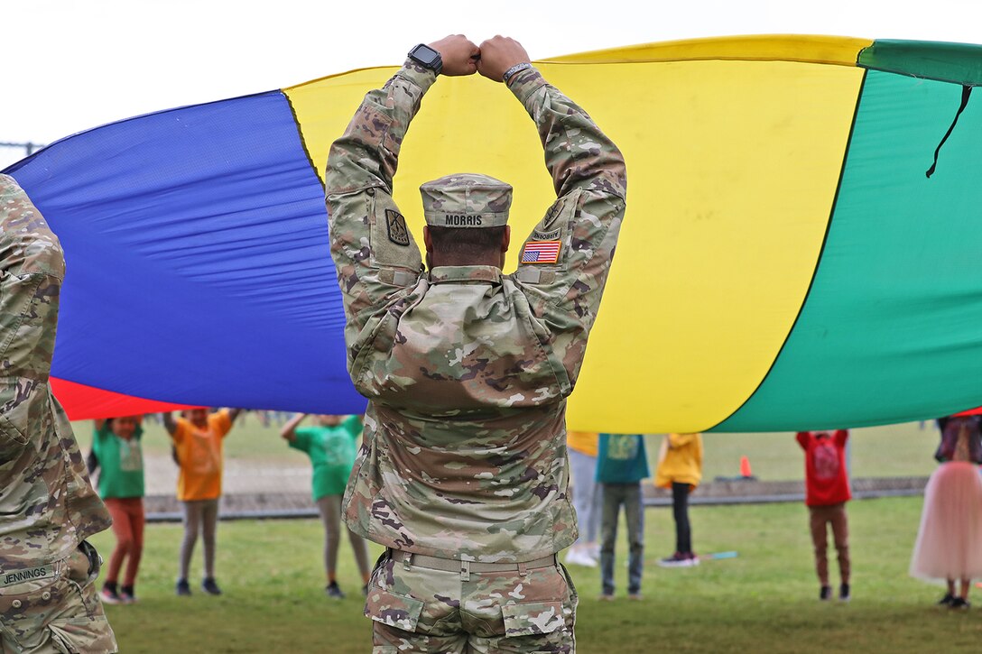 Service members and students stand in a circle to hold up a large multicolored tarp.