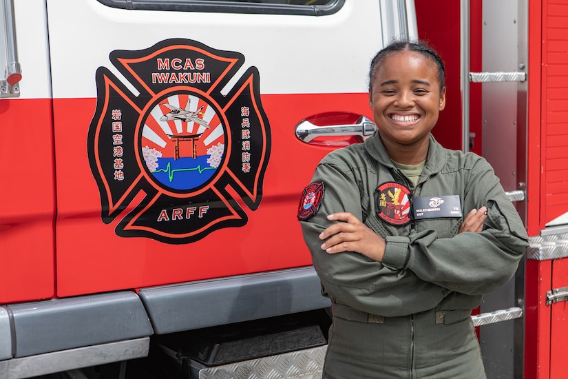 A service member smiles for a photo while standing in front of a fire truck.