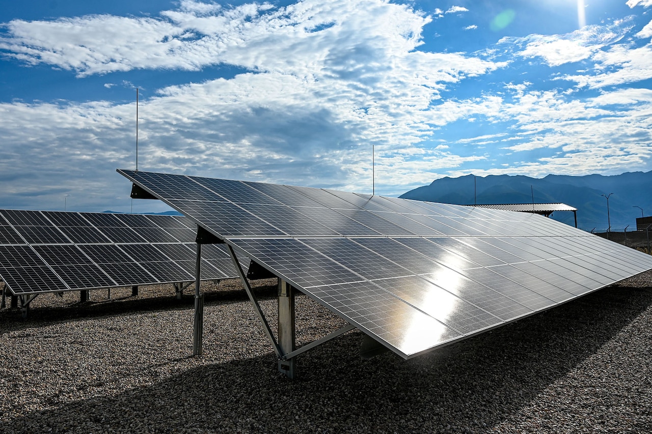 A line of solar panels reflect the sun on a partly cloudy day.