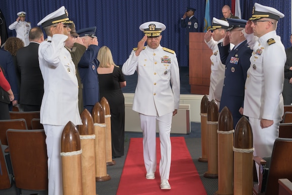A Naval Admiral salutes as he passes down a red carpet through a joint military group of sideboys